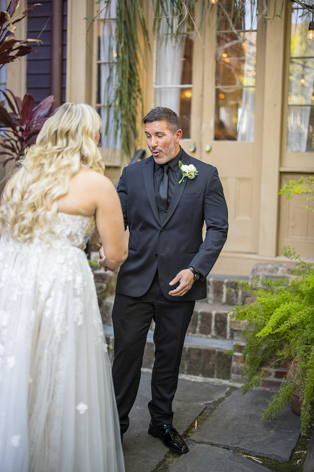 Groom in his black suit reacts to seeing his bride in her white dress at during their first look at the Seraphim House in New Orleans, Louisiana. 