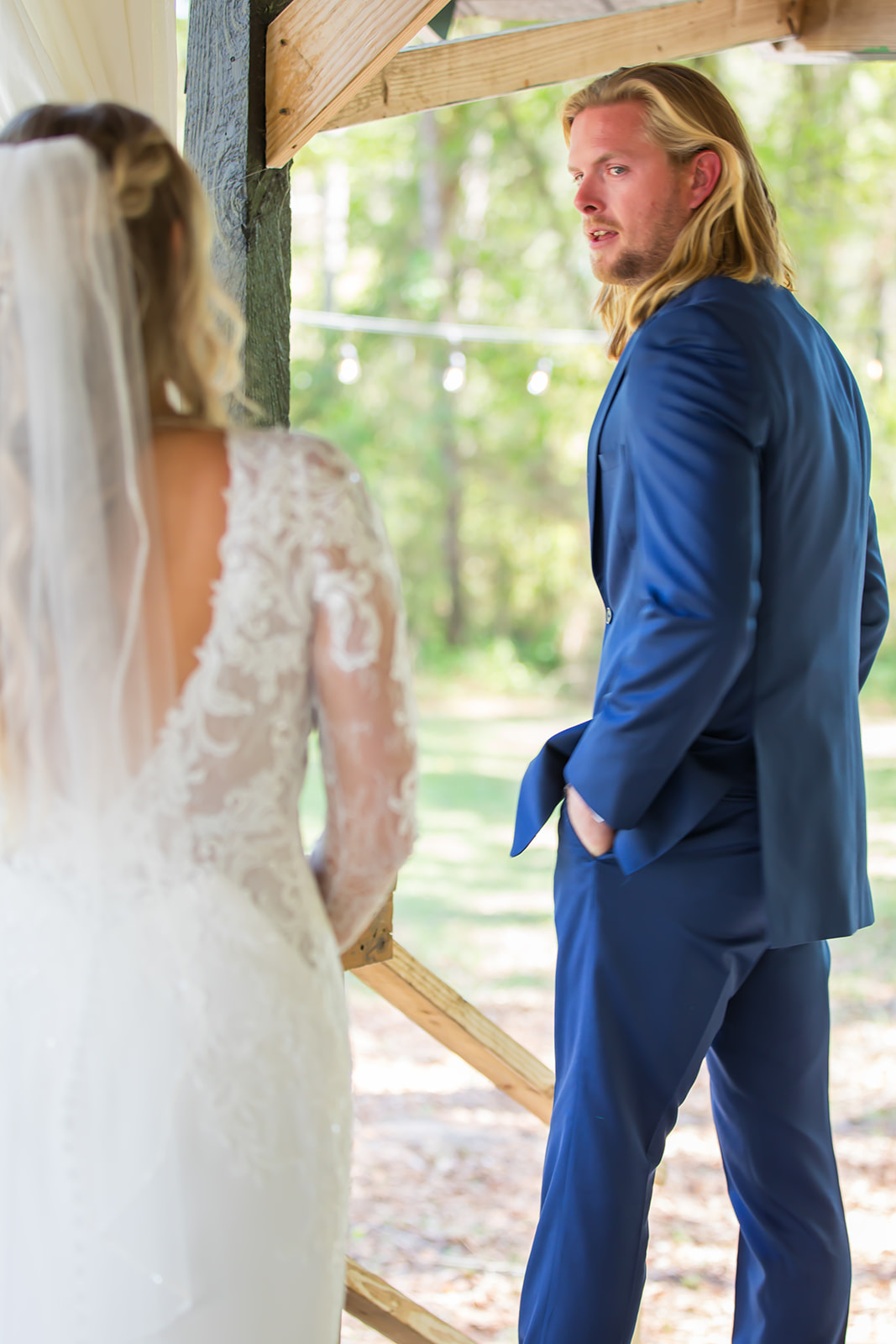 Groom in his blue suit turns to sees his bride for the first time in her white wedding dress.