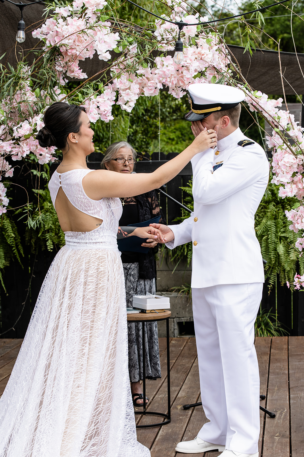 Bride in white dress consoling her husband as he is brought to tears at the altar